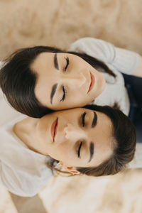 Young female twins with eyes closed on sand