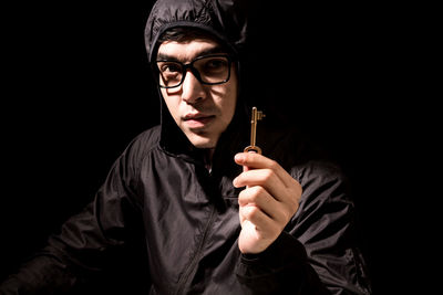 Portrait of criminal holding key against black background