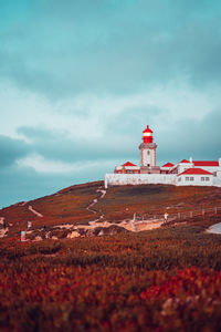 Lighthouse on field by building against sky