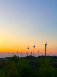 Wind turbines on field against sky during sunset