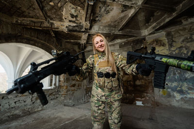 Caucasian woman in army uniform holding two machine guns. 