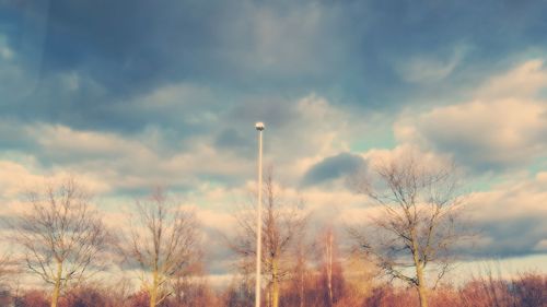 Low angle view of bare trees against cloudy sky