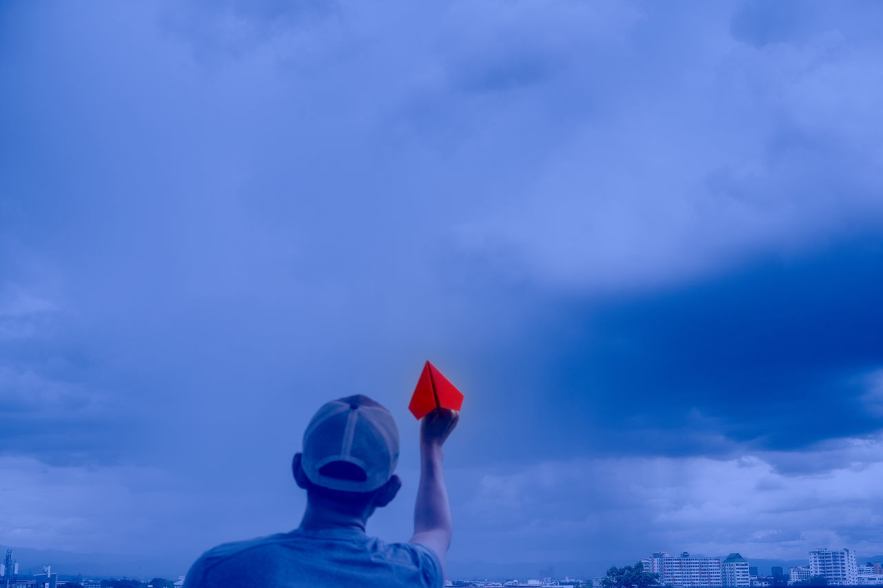 REAR VIEW OF MAN HOLDING UMBRELLA AGAINST SKY