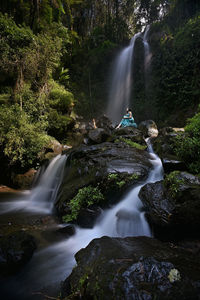 Woman and waterfalls flowing through rocks in forest