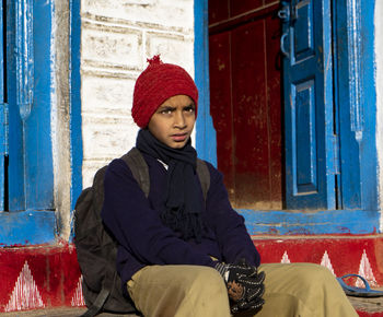 Portrait of young woman sitting against wall