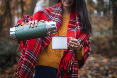 Midsection of woman pouring drink from insulated drink container in forest