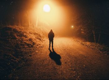 Rear view of silhouette man walking on illuminated street at night