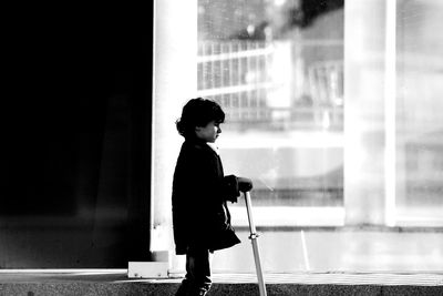 Side view of boy riding push scooter against window