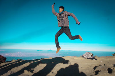 Full length of man jumping at beach against blue sky