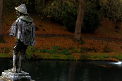 Rear view of man standing by statue during rainy season