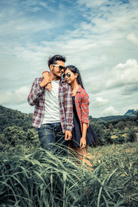 Young couple standing by plants against sky