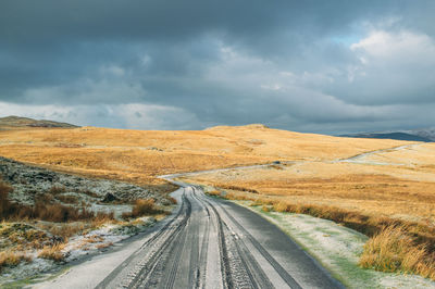 Road passing through field against cloudy sky