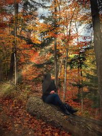 Woman sitting on log in forest during autumn