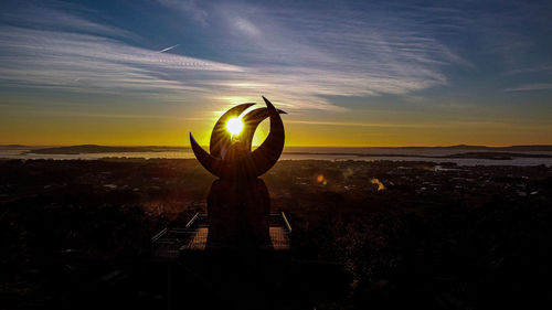 Silhouette sculpture on landscape against sky during sunset