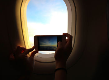 Cropped image of person photographing sky through airplane window