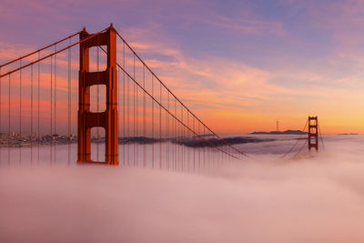 Suspension bridge over river against sky during sunset