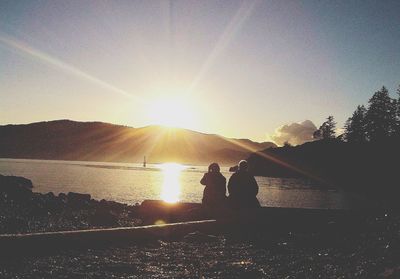 Silhouette people on shore against sky during sunset