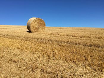 Hay bales on field against clear blue sky