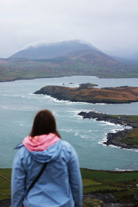 Rear view of woman in blue jacket looking at sea against sky