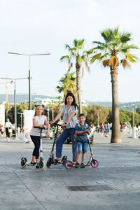 Happy family lifestyle. mother, boy, girl in city. ride scooters. laughing on a summer. fun