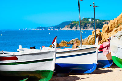 Boats moored on beach against blue sky