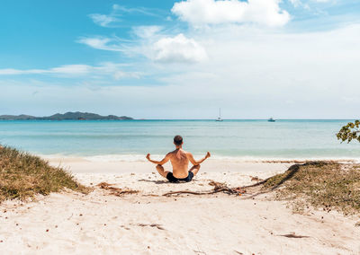 Rear view of shirtless man sitting on beach