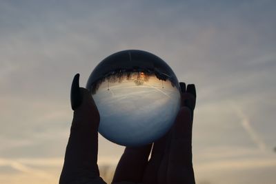 Silhouette hand holding crystal ball with reflection against sky