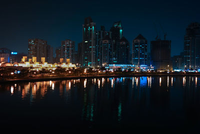 River by illuminated buildings against sky at night