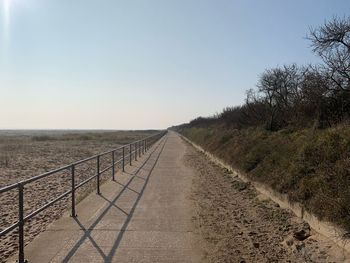 Empty road amidst field against clear sky