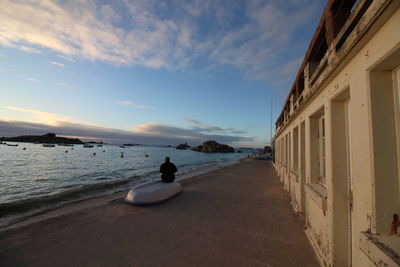 Rear view of man sitting on moored boat at beach against sky