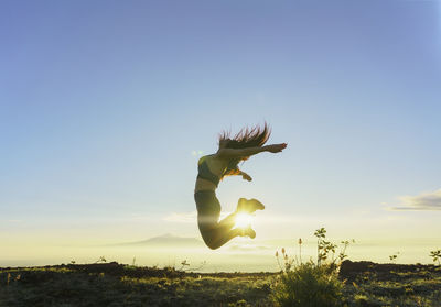Low angle view of woman with arms outstretched standing on field against sky during sunset