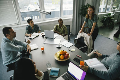 Businesswoman discussing in brainstorming session with multiracial colleagues at desk in office