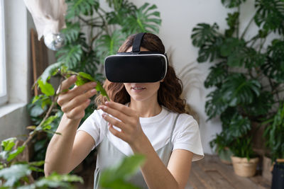 Home gardening, metaverse. woman using vr glasses in greenhouse, touching plant. augmented reality.