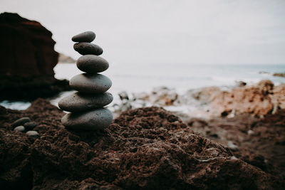 Stack of stones on rock at beach against sky