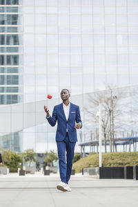 Businessman playing with apple walking on footpath