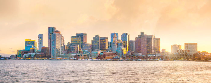 Sea by modern buildings against sky during sunset