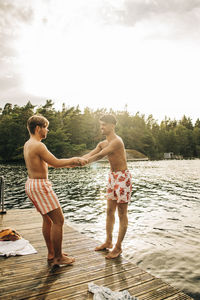 Male friends holding hands while standing on jetty during vacation