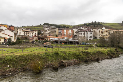 Buildings by river against sky in city