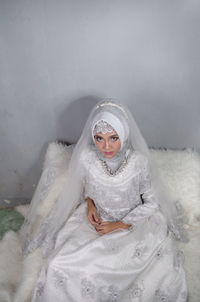 Portrait of bride wearing traditional clothing sitting against wall