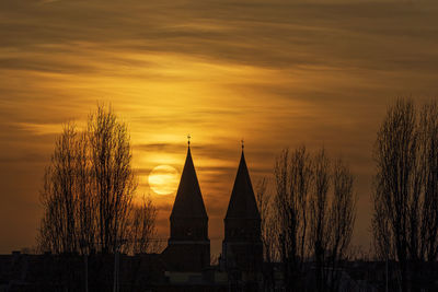 Silhouette of trees and building against sky during sunset