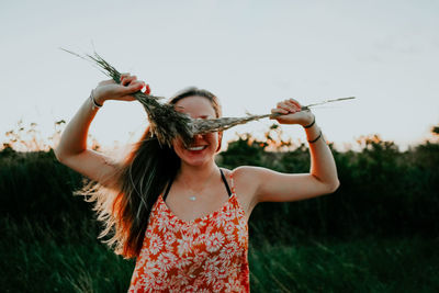 Woman holding plant against sky