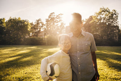 Portrait of father and son with ball standing on grassy field