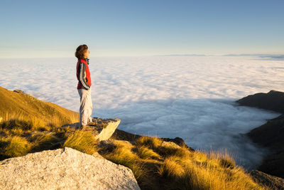 Side view of female hiker standing by cloudscape on mountain