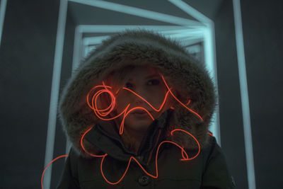 Woman in hooded clothing with light painting standing against illuminated lights