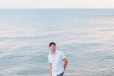 Smiling man looking away while standing against sea