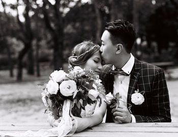 Groom kissing on bride forehead against trees