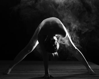 Naked woman bending against black background