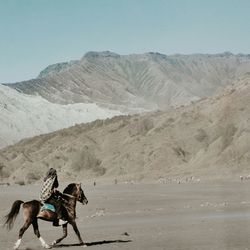 Man riding horse in desert against mountains
