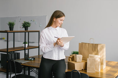 A cute girl makes notes in a notebook next to eco packages on the table