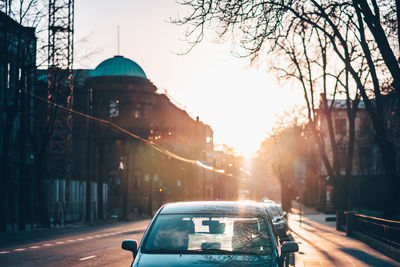 Cars on city street against sky during sunset